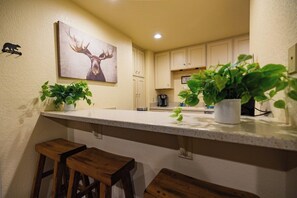 A kitchen with a white countertop, wooden stools, a coffee machine, and potted plants. - Pet Friendly 1BD 1BA Mammoth Retreat (Mammoth Lakes)