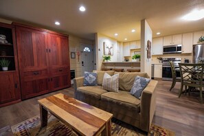A living room with a sofa, a wooden coffee table, and a kitchen in the background. - Pet Friendly 1BD 1BA Mammoth Retreat (Mammoth Lakes)
