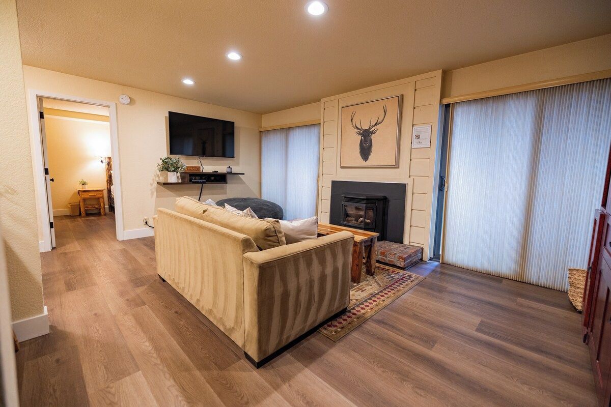 A living room with a sofa, a fireplace, a mounted TV, and a wall-mounted deer head artwork.