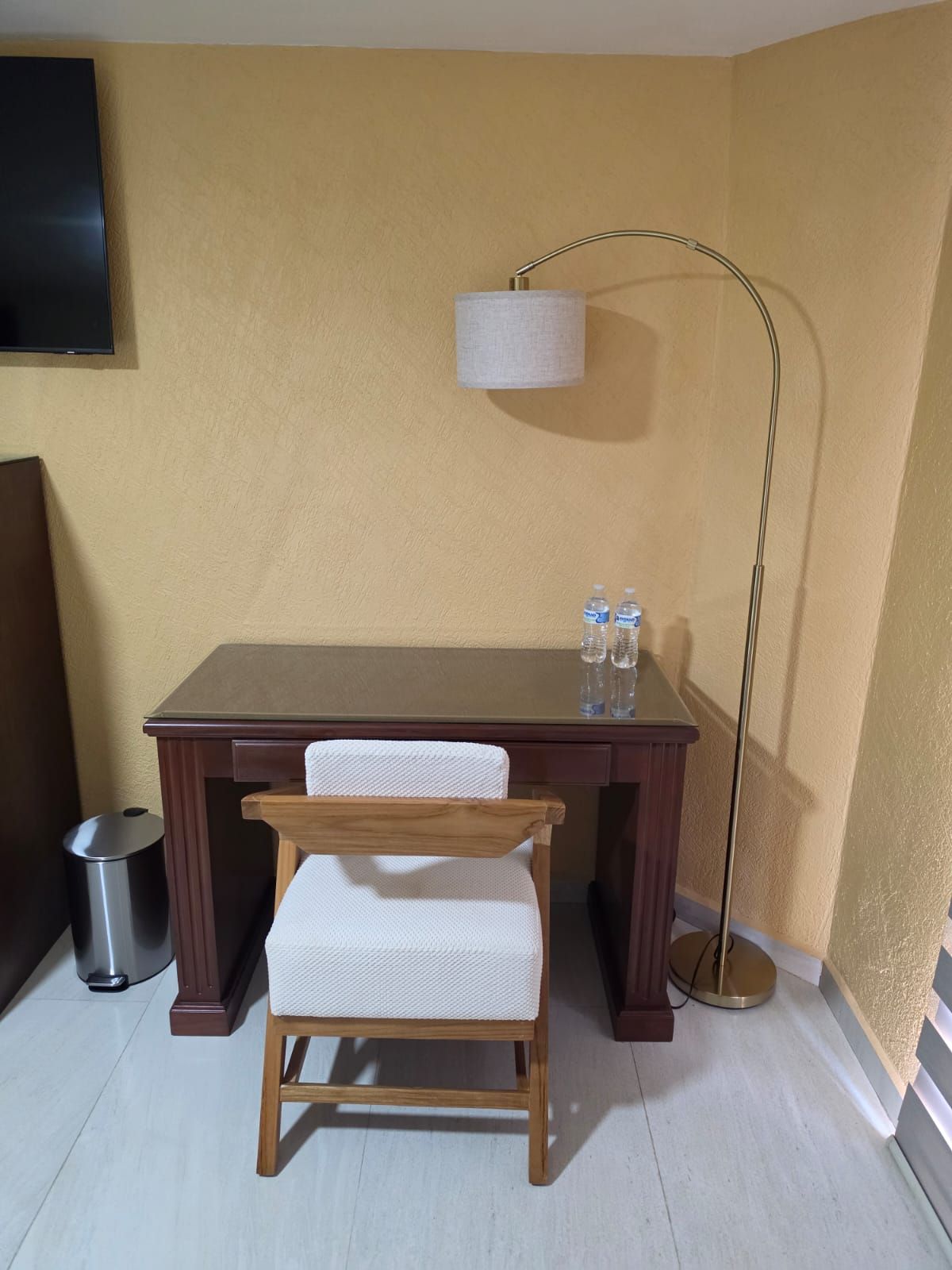 A small room with a wooden desk, a chair, a floor lamp, and a trash can.