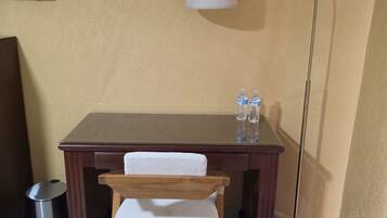 A small room with a wooden desk, a chair, a floor lamp, and a trash can.