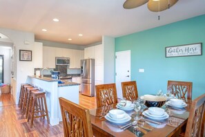 A modern kitchen with a central island, wooden bar stools, and a dining area set for six with a glass table. - Waikoloa Colony Villas - 6 BR (2 townhomes), Sleeps 12 (Waikoloa Village)