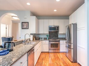 A modern kitchen with white cabinets, stainless steel appliances, granite countertops, and wooden flooring. - Waikoloa Colony Villas - 6 BR (2 townhomes), Sleeps 12 (Waikoloa Village)