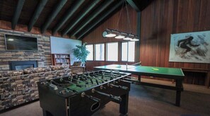 Ett rum med ett fotbollsspel, en soffa, en bokhylla, en öppen spis och ett stort fönster.