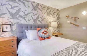 A hotel room with a bed, a nightstand, a lamp, and a wall-mounted clock. - Updated Pet Friendly Slope Side 2BD 2BA Condo (Mammoth Lakes)
