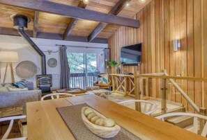 A wooden interior with a dining table, chairs, a television mounted on the wall, and a window with a view of trees. - Updated Pet Friendly Slope Side 2BD 2BA Condo (Mammoth Lakes)
