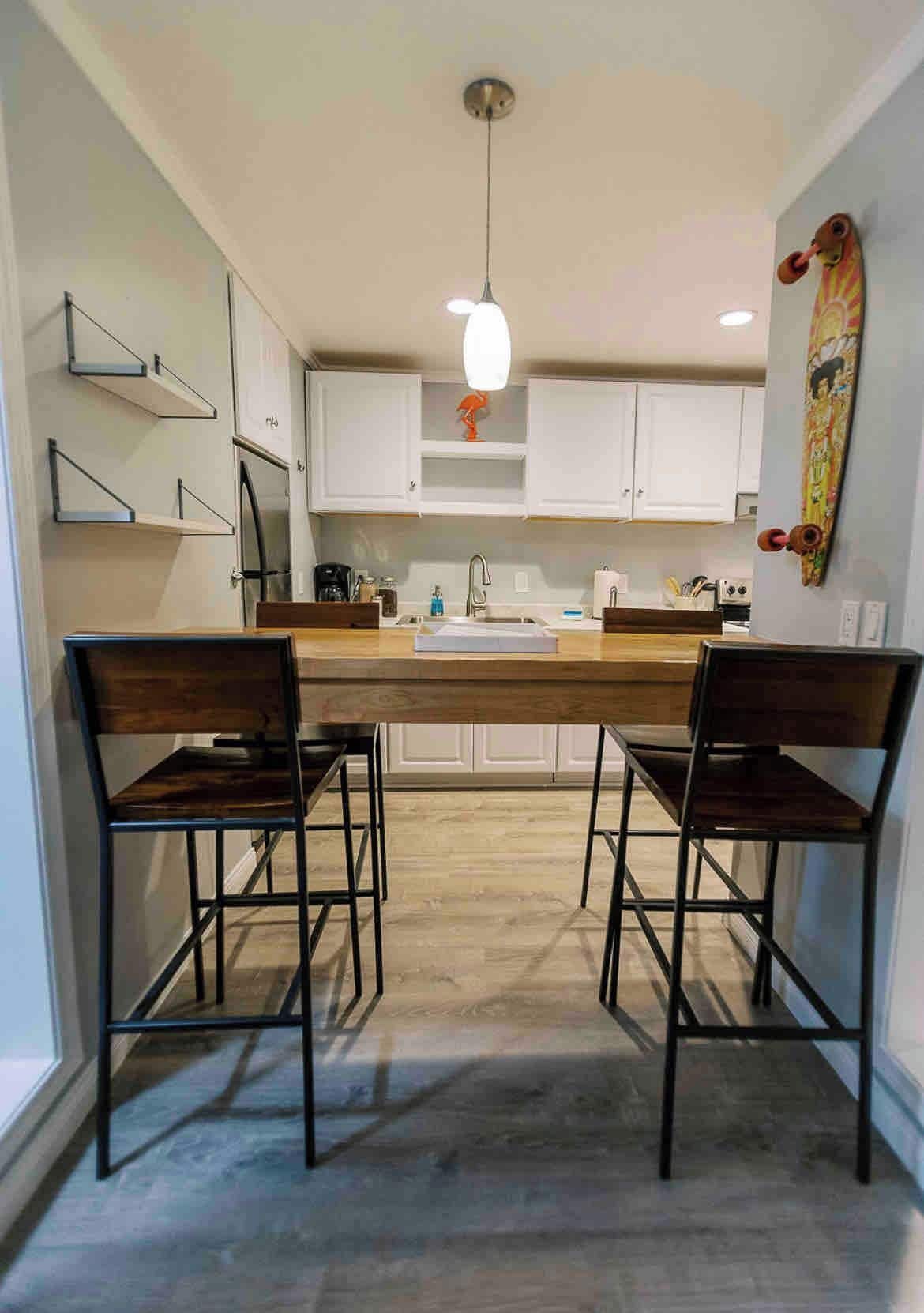 A modern kitchen with a central island, two bar stools, and a pendant light.