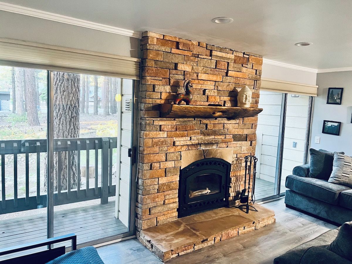 A stone fireplace with a mantel shelf, a glass door leading outside, and a grey sofa in the foreground.