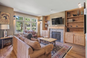 A cozy living room with a fireplace, a television, and a bookshelf. - Mammoth Pet Friendly 2BD 2BA W/ Spectacular Views (Mammoth Lakes)