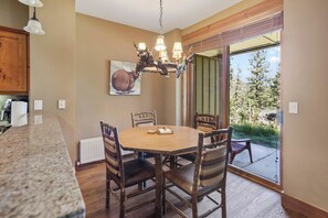 A dining area with a round table, chairs, a chandelier, and a view through a glass door. - Mammoth Pet Friendly 2BD 2BA W/ Spectacular Views (Mammoth Lakes)