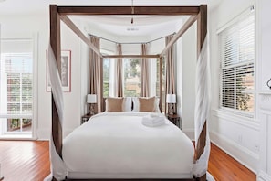 A four-poster bed with a canopy, two bedside lamps, and a view through the windows. - The Lyons Estate | Historic Savannah Luxury (Savannah)