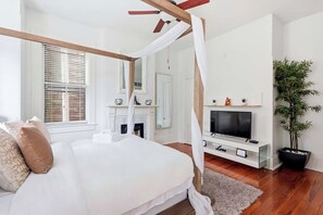A bedroom with a four-poster bed, a television, a fireplace, and a potted plant. - The Lyons Estate | Historic Savannah Luxury (Savannah)