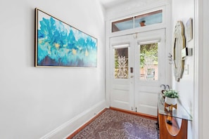 A hallway with a white door, a framed abstract painting, a glass cabinet with a plant, and a patterned rug. - The Lyons Estate | Historic Savannah Luxury (Savannah)