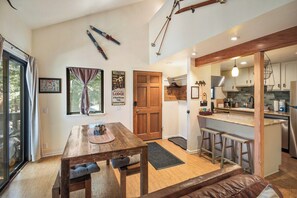 A modern kitchen with a bar area, wooden dining table, and ski equipment on the wall. - Gorgeous Hidden Valley Loft w/ a view (Mammoth Lakes)