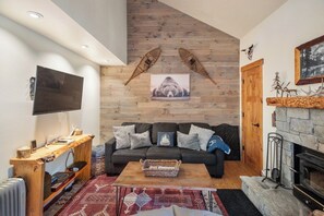 A cozy living room with a fireplace, a television mounted on the wall, and a wooden ceiling. - Gorgeous Hidden Valley Loft w/ a view (Mammoth Lakes)