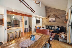 A modern kitchen with a stainless steel refrigerator, wooden bar stools, and a dining table with a woven placemat. - Gorgeous Hidden Valley Loft w/ a view (Mammoth Lakes)