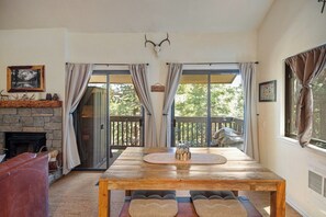 Ein gemütliches Zimmer mit Kamin aus Stein, einem Holztisch mit Kissen und einem großen Fenster mit Vorhängen.
