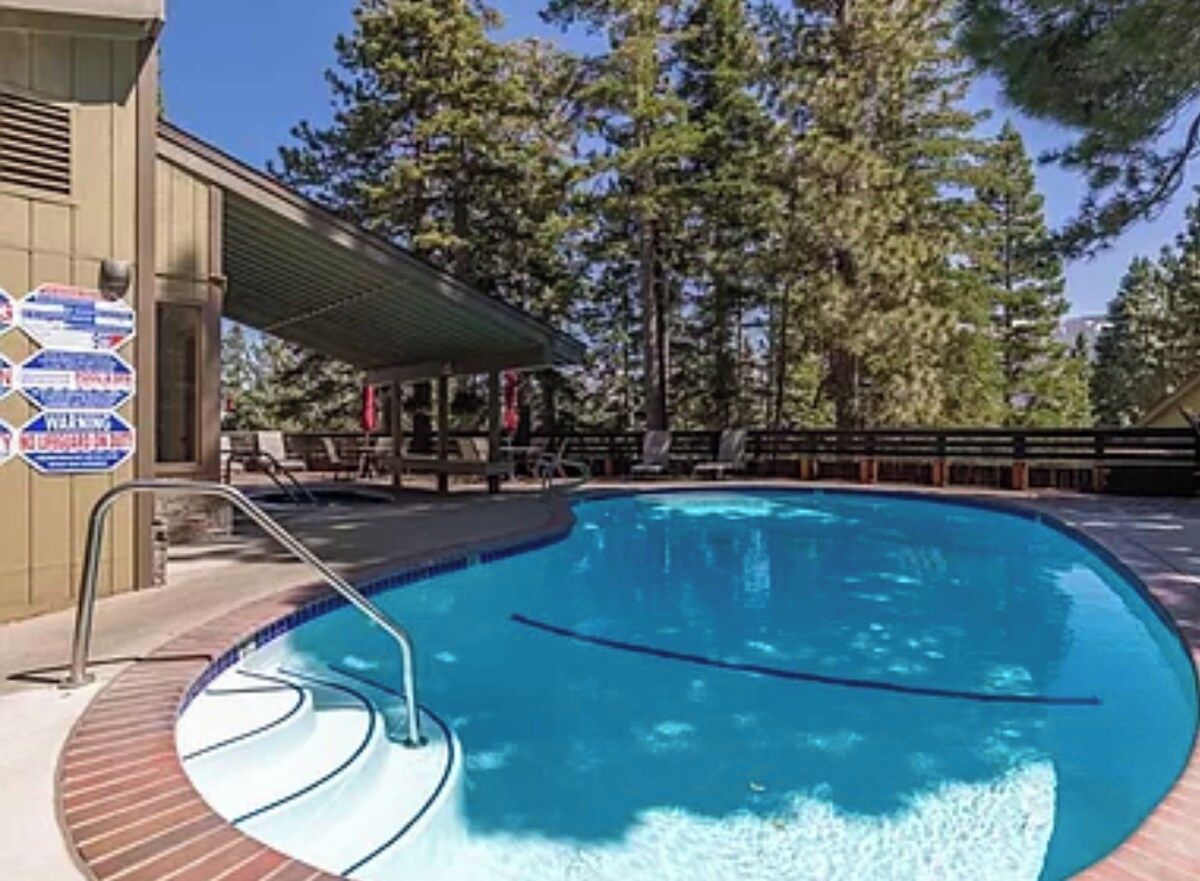A swimming pool with a metal ladder and a covered seating area with lounge chairs.
