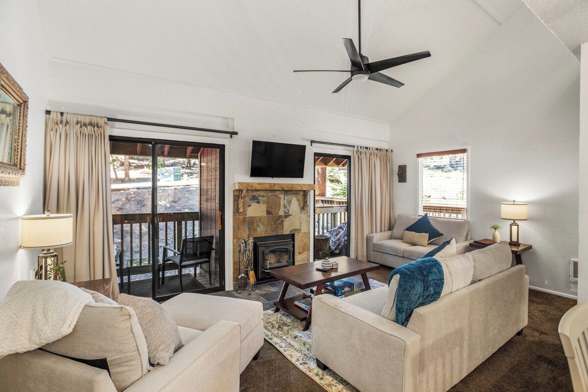 A living room with a fireplace, a ceiling fan, and a TV mounted on the wall.