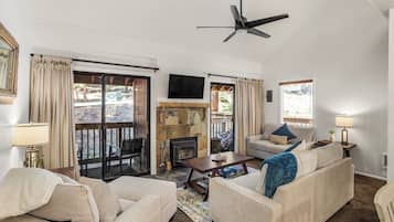 A living room with a fireplace, a ceiling fan, and a TV mounted on the wall.