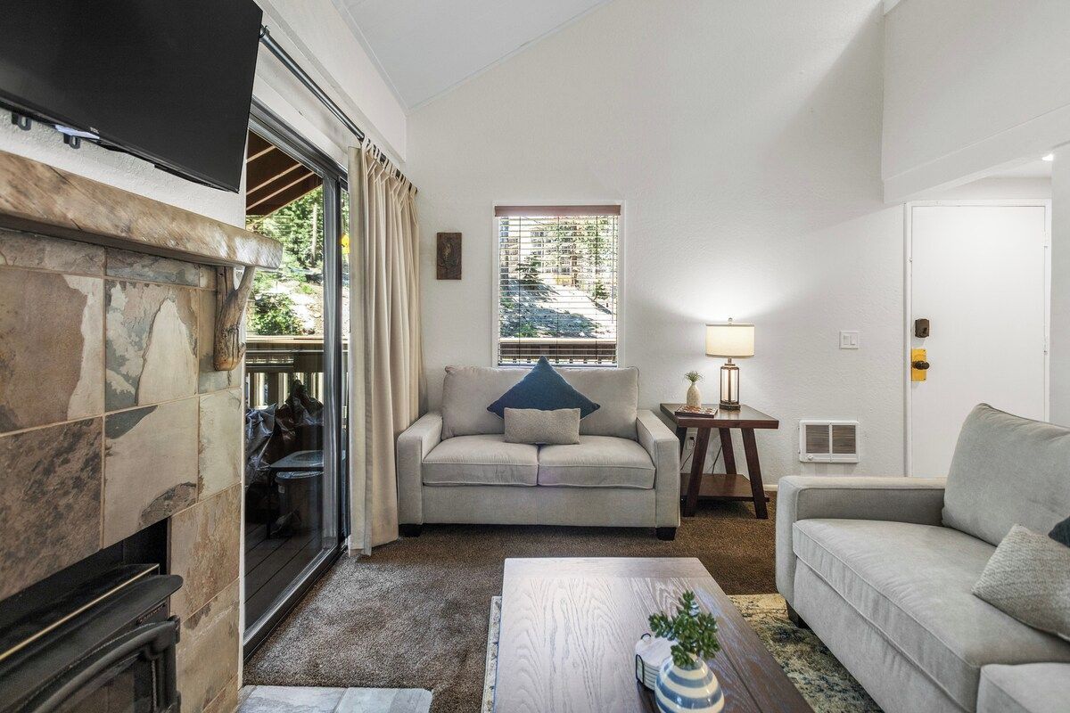 A living room with a fireplace, a sofa, a coffee table, and a window with blinds.