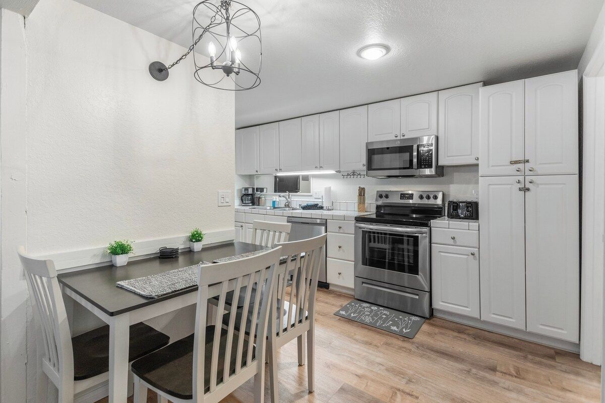 A modern kitchen with white cabinets, stainless steel appliances, and a dining area with a table and chairs.