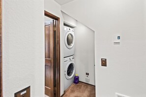 Ein Waschraum mit einer Waschmaschine und einem Trockner nebeneinander, einer Tür mit der Aufschrift 'ENTRY' und einer kleinen Flasche auf dem Boden.
