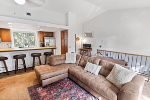 Ein modernes Wohnzimmer mit einem braunen Ledersofa, einem gemusterten Teppich und einer Küche im Hintergrund.