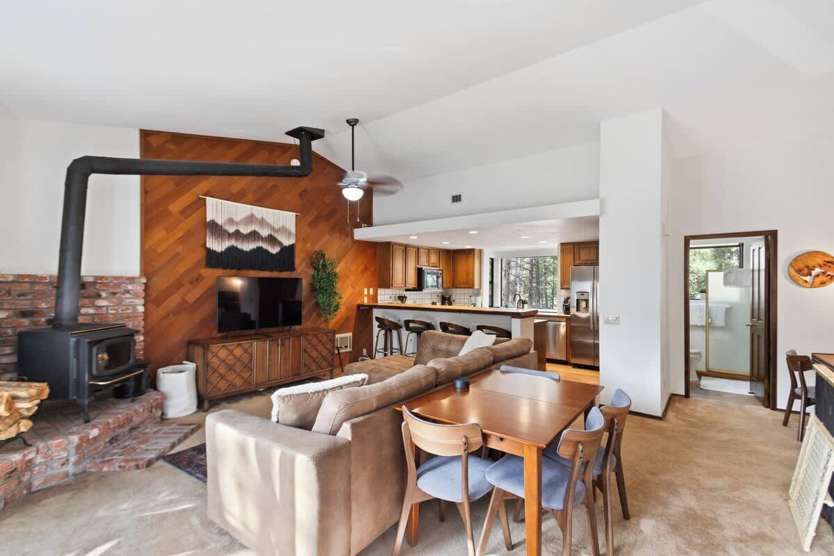 A modern living room with a fireplace, a dining area, and a kitchen in the background.