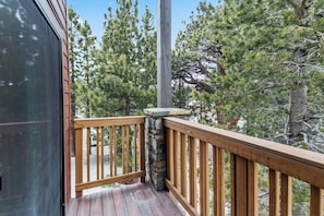 A wooden deck with a stone pillar, surrounded by pine trees. - Premier Slope Side Pet Friendly  2bd+Loft (Mammoth Lakes)
