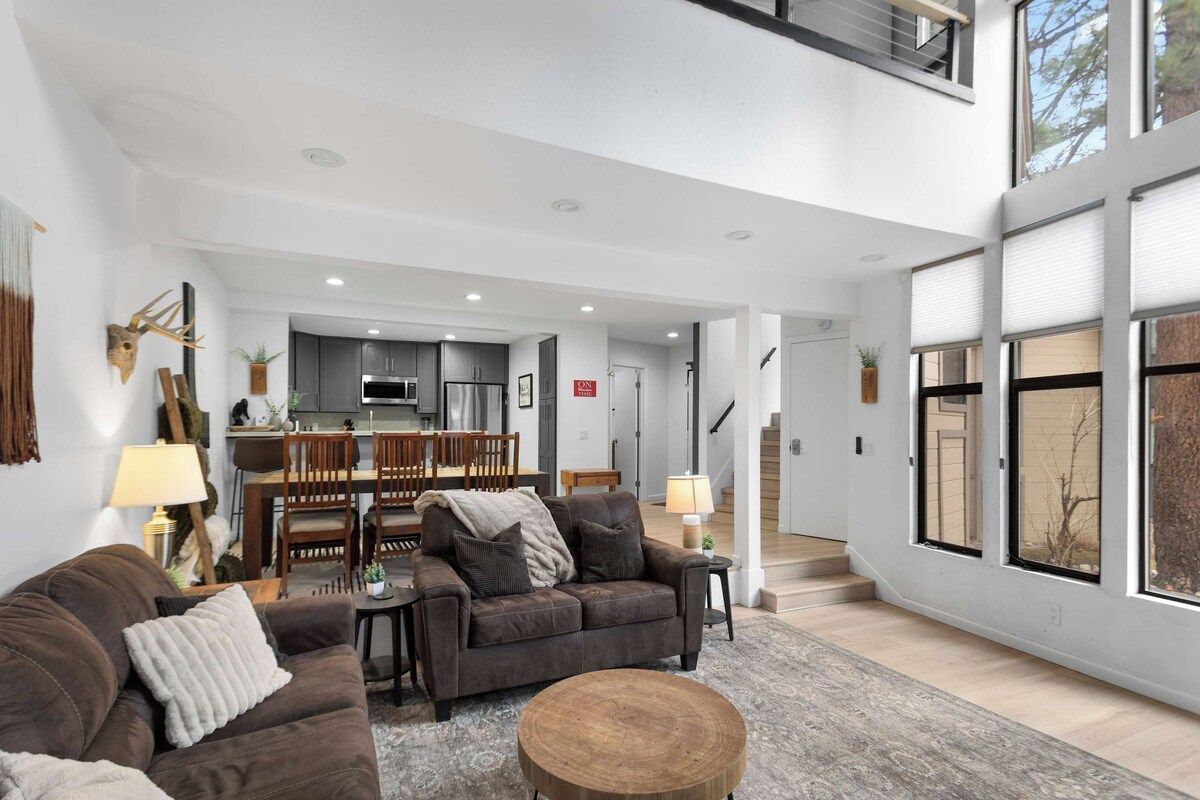 A spacious living area with a sofa, a coffee table, and a dining area in the background.