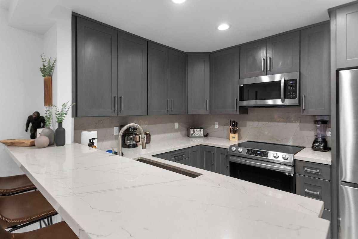 Une cuisine moderne avec des meubles gris, un four à micro-ondes en acier inoxydable, une cuisinière et un réfrigérateur.