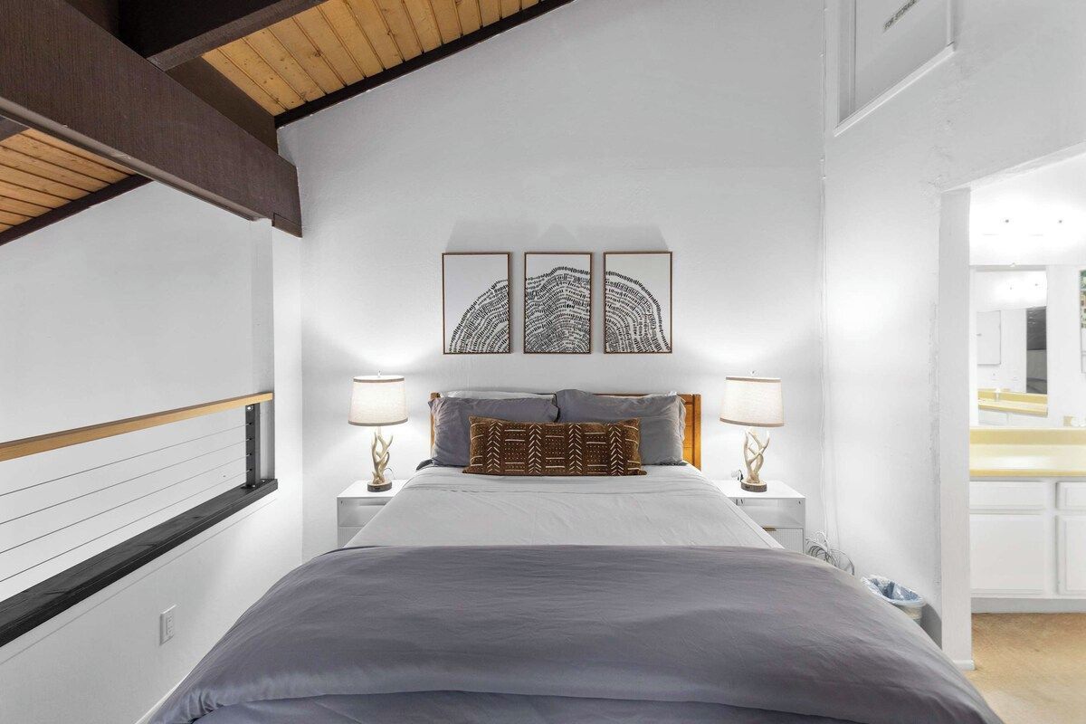 Une chambre à coucher comprenant un lit, deux tables de chevet, une tête de lit et une œuvre d’art accrochée au mur.
