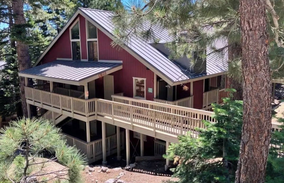 A two-story cabin with a balcony and a metal roof, surrounded by trees.