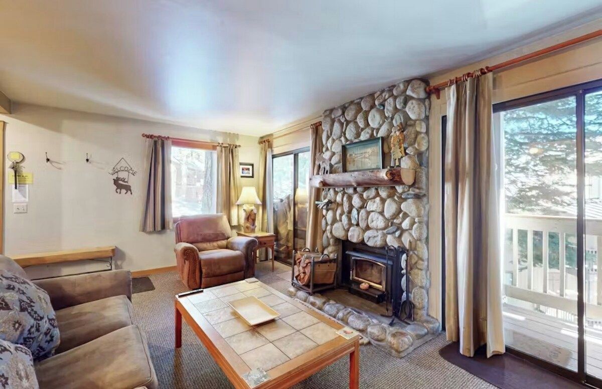 Ein gemütliches Wohnzimmer mit Kamin aus Stein, einem Ledersessel und einer Couch.
