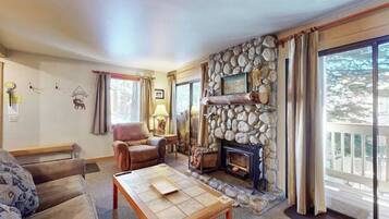 Ein gemütliches Wohnzimmer mit Kamin aus Stein, einem Ledersessel und einer Couch.