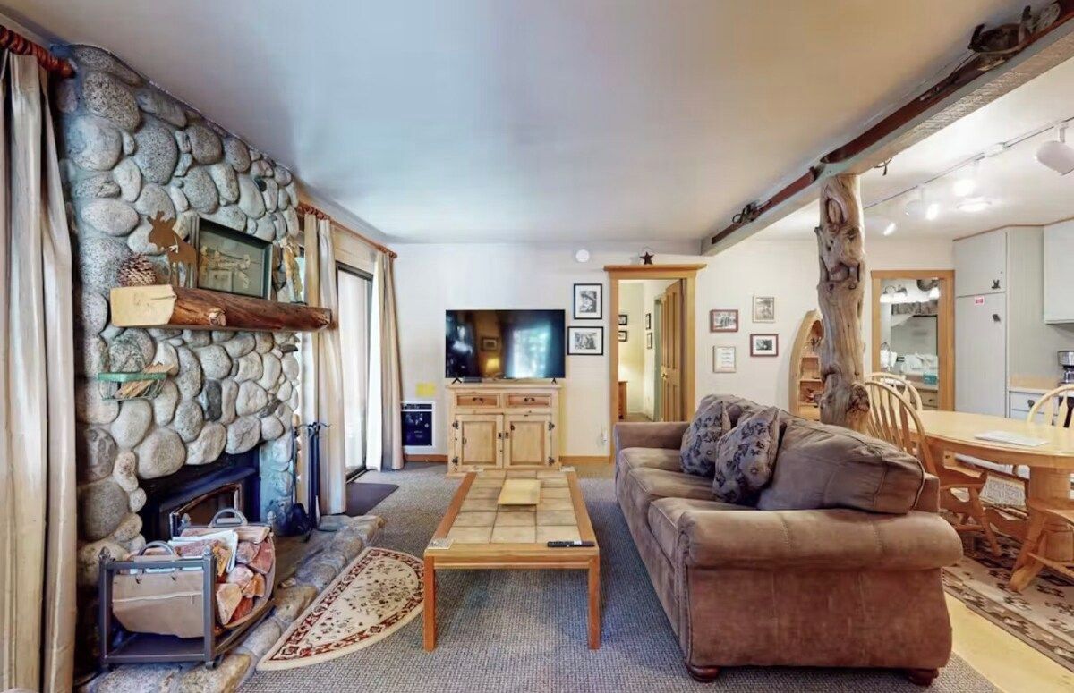 Ein gemütliches Wohnzimmer mit Kamin aus Stein, einem Fernseher, einer Couch und einem Essbereich.