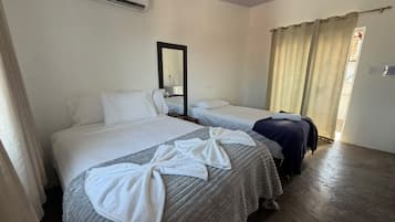 A hotel room with two beds, a mirror, a window with curtains, and a suitcase.