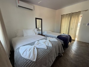 Habitació d'hotel amb dos llits, un mirall, una finestra amb cortines i una maleta.