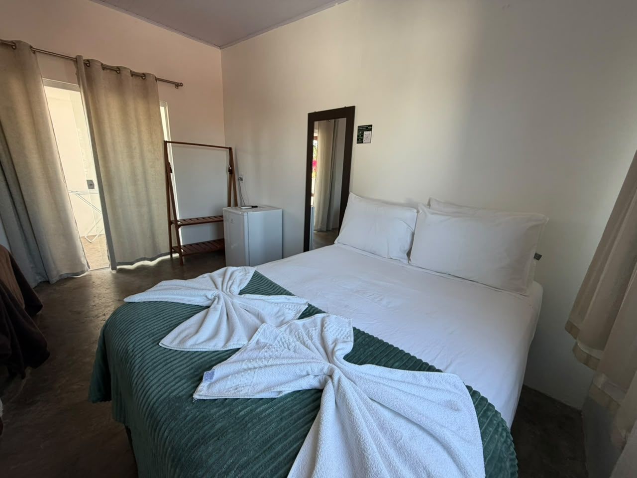 A hotel room with a bed, a bedside table, a mirror, and a door.