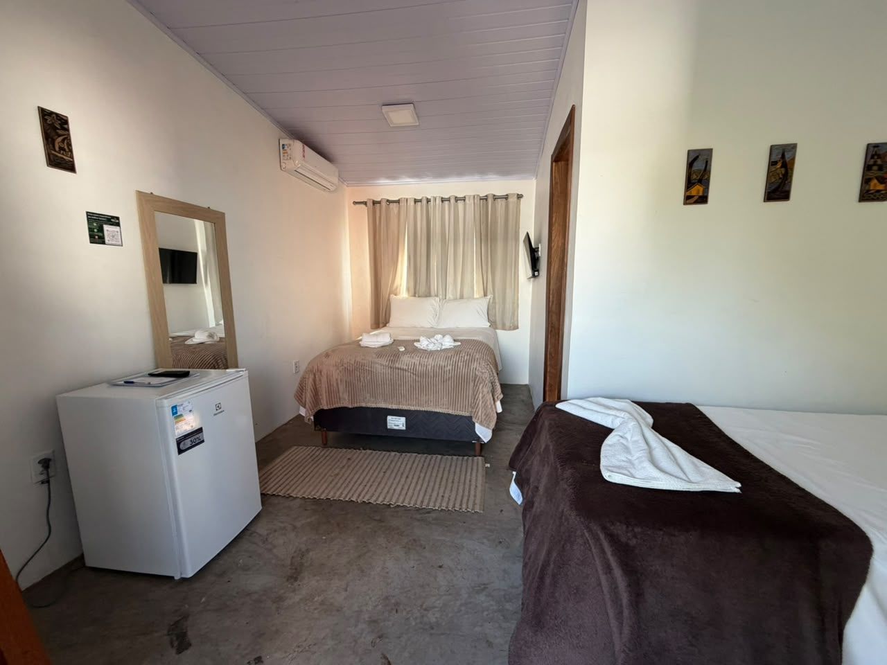 A bedroom with a bed, a bedside table, a refrigerator, and a window with curtains.