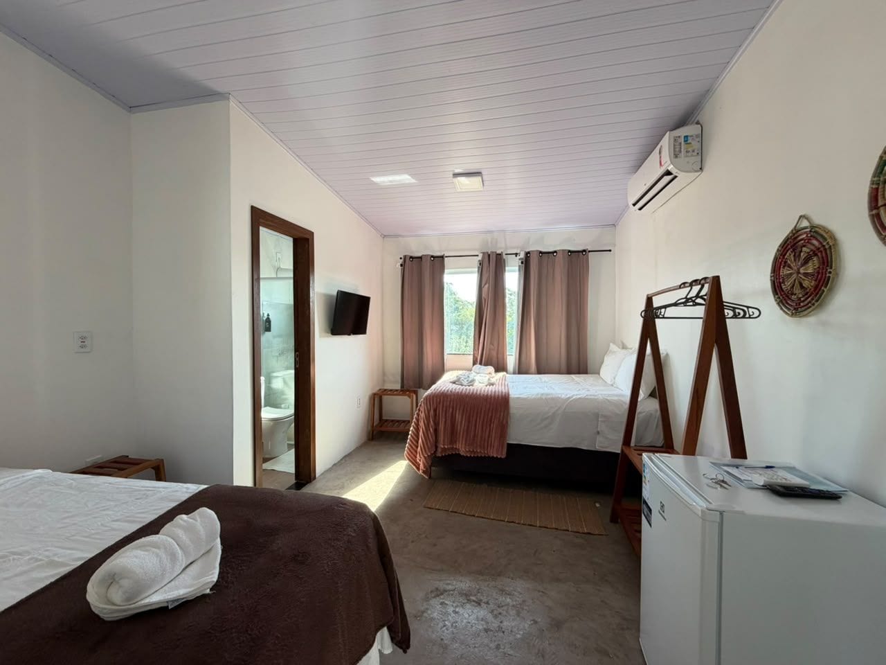 A hotel room with two beds, a small table, a refrigerator, and a television on the wall.