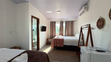 A hotel room with two beds, a small table, a refrigerator, and a television on the wall.