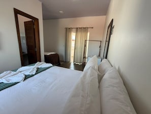 A hotel room with a large bed, a wooden door, a window with curtains, and a bedside table. - VILA DO RIO (Santo Amaro do Maranhão)