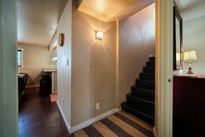 Un couloir avec un escalier, un luminaire fixé au mur et un tapis sur le sol.