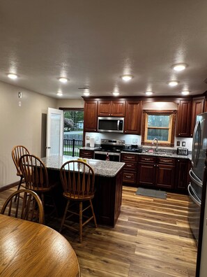Una cocina con armarios de madera, microondas, refrigerador y un comedor con sillas.