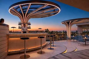 Eine Bar im Freien mit einer Sitzgruppe in Kreisform, einem Barkeeper und Blick auf die Stadtlandschaft.