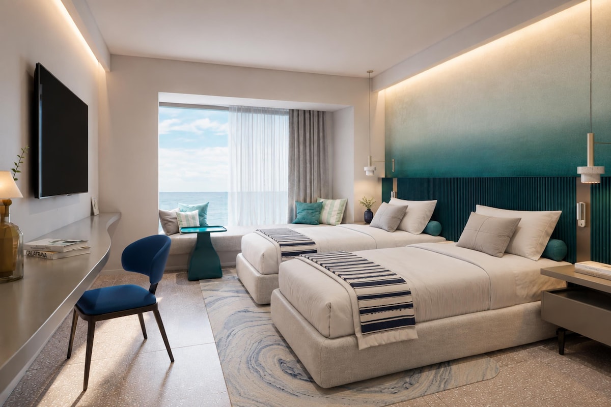 Ein modernes Hotelzimmer mit einem großen Bett, einem Schreibtisch, einem Stuhl und Meerblick.