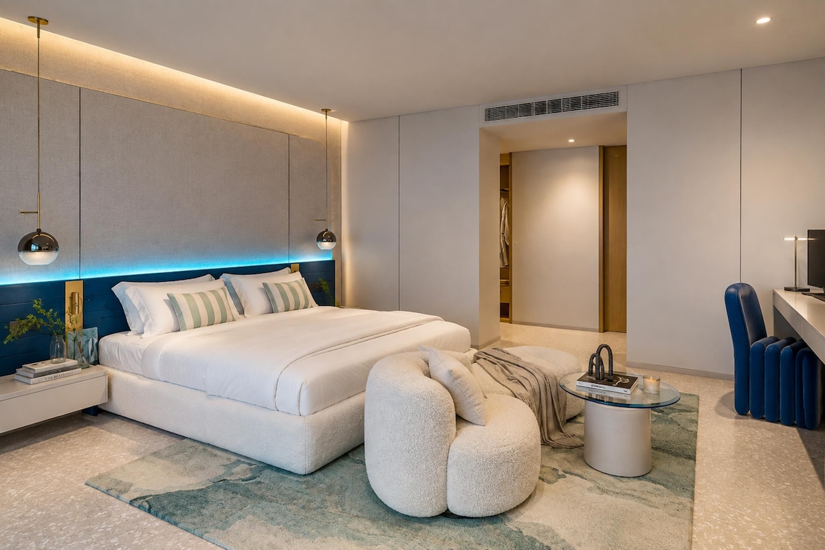 Ein modernes Schlafzimmer mit einem großen Bett, Nachttischen, einer Leselampe, einem Glastisch und einem blauen Sessel.