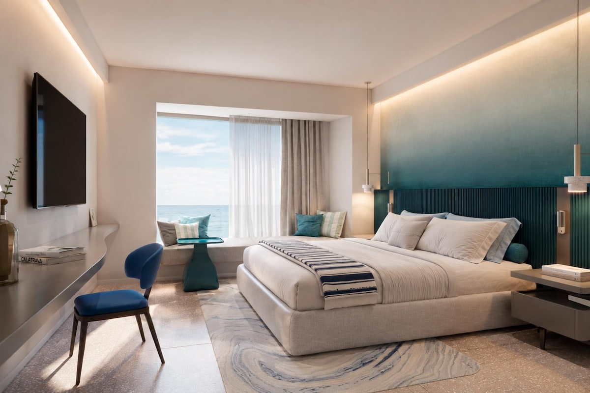 Ein modernes Hotelzimmer mit Bett, Schreibtisch, Stuhl, Fernseher und Meerblick.